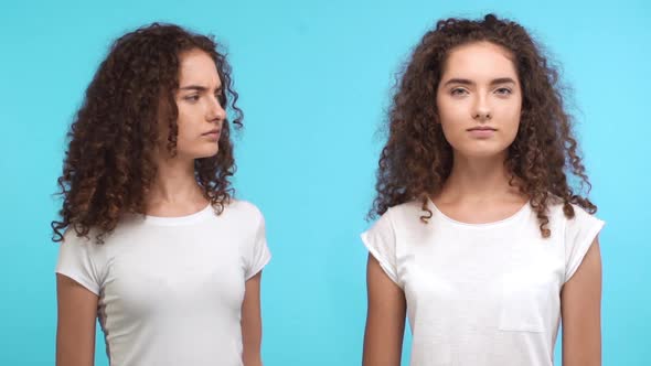 Two Beautiful Young Curly Female Twins Touching Each Other Hair Smiling with Arms Folded on Blue