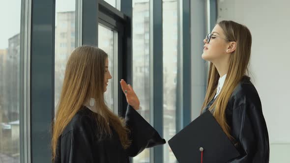 Two Young Happy Graduates Communicate Happily By the Window