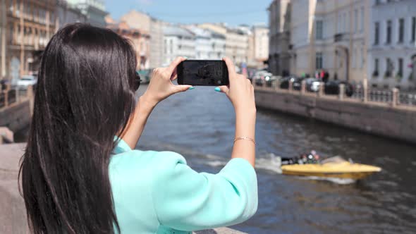 Tourist Woman Taking Photo Using Smartphone of Floating Boat River Surrounded By Historic City