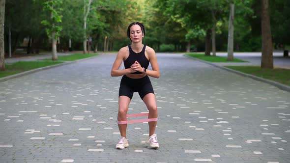 Front View of Stylish Woman with Dreadlocks Makes Crounchy Side Steps with Pink Rubber Band on Legs