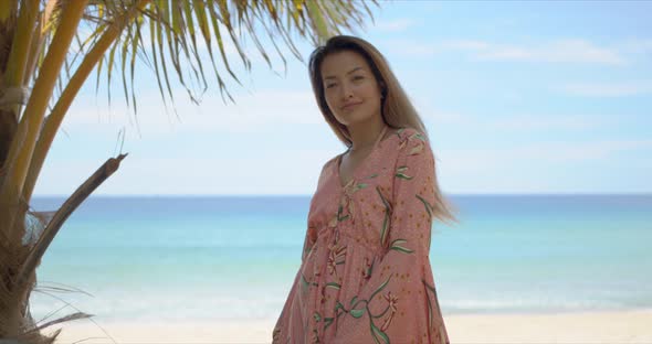 Cheerful Ethnic Female Standing Near Palm on Beach