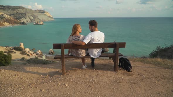 Young Hugging Couple Is Sitting on a Bench on a Cliff with a Gorgeous Picturesque View of the