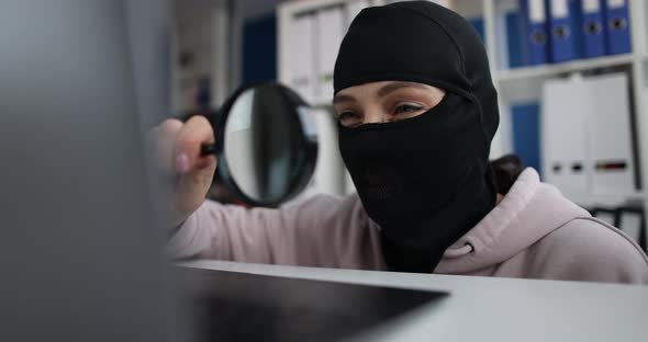 A Woman in Mask Looks Into Laptop Through Magnifying Glass