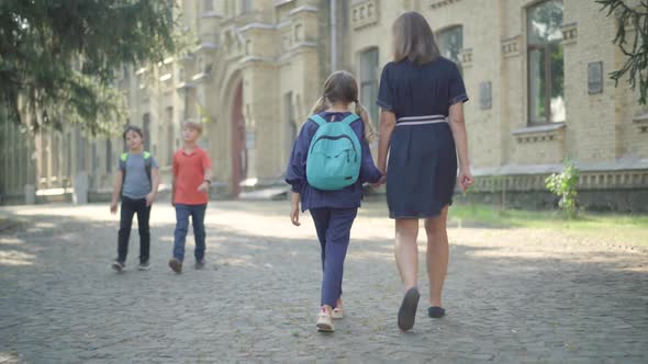 Wide Shot of Mother and Daughter Walking Along Sunny Schoolyard and Talking. Back View of Positive