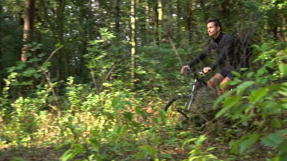 A Cyclist Rides Down a Path Through a Forest - Side View