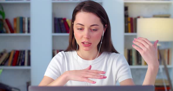 Attractive Young Caucasian Woman in Headset and Mic Sits on Table Indoors Talking Seriously 