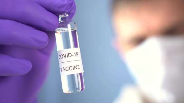 A doctor in protective gloves and a face mask holds an ampoule with a medicine for coronavirus