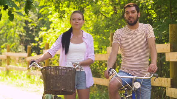 Happy Couple with Bicycles Talking at Summer Park