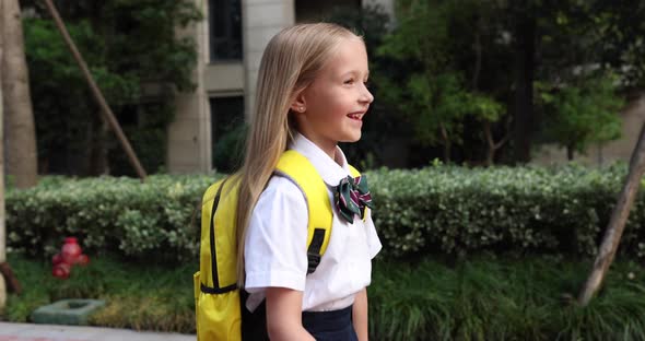 Happy Little Caucasian Blonde Girl Seven Years Old in Uniform with Yellow Backpack Going Back to