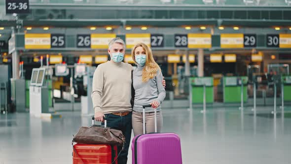 Happy Mature Couple of Travellers Standing with Suitcases at Airport Building Wearing Protective