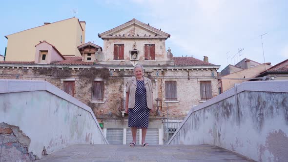 Senior Woman Stands on Bridge Against Historical Building