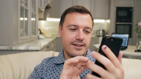 Young Adult Man Relaxing on Comfortable Couch Using Mobile Application Scrolling in Social Network