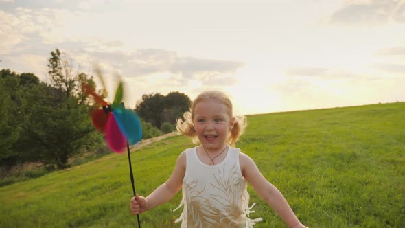 Little Smiling Girl Having Fun Running on the Meadow with a Toy Windmill