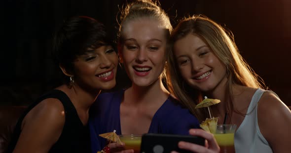 Smiling friends taking a selfie from mobile phone while having cocktail