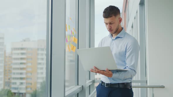 A Young Man Holds a Tablet in His Hands and Stands By the Window. Remote Work at Home and Work in a