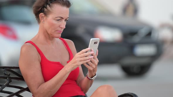 Mature Happy Tourist Woman Using Phone While Sitting On The Bench