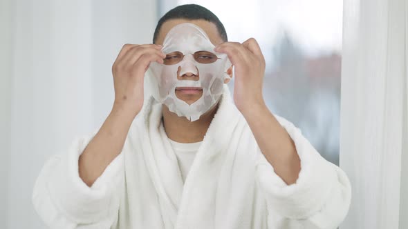 Portrait of Confident Handsome African American Man Taking Off Moisturizing Facial Mask Looking at