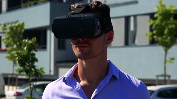 Young Handsome Man Uses Virtual Reality Glasses - Buildings in the Background - Closeup