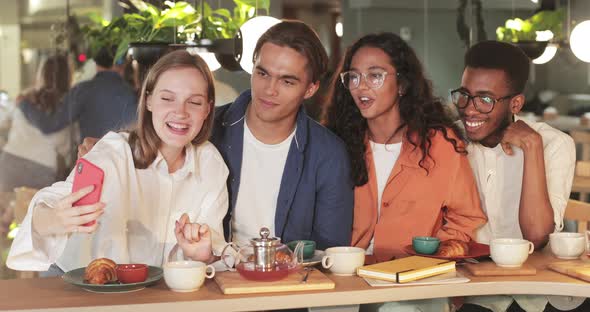 Young People Laughing and Waving While Posing for Selfie in Cosy Restaurant. Happy Girl Holding