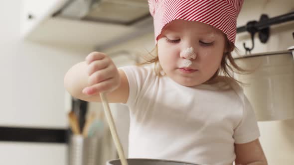 Portrait of Baby Girl in Chief Hat Having Fun While Cooking in Kitchen and Playing with Flour