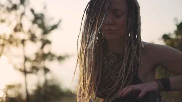 Beautiful Young Hippie Woman with Dreadlocks Playing on Djembe