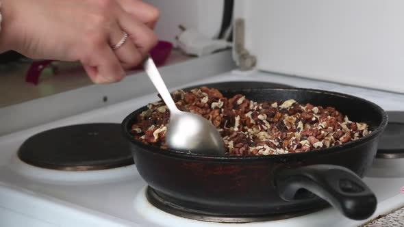 A Woman Prepares Kozinak From Nuts. Roasts Sunflower Seeds, Peanuts And Walnuts In A Pan