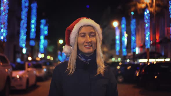 A beautiful woman in a Santa Claus hat walks at night on Christmas