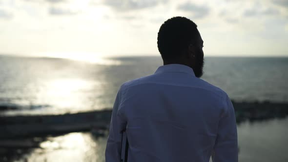 Back View of African American Male Tourist Standing in Sunlight at Sunset Admiring Beauty of
