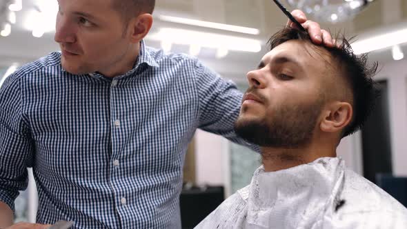 Unparalleled Barber with a Beard and a Tattoo Is Cutting the Hair of His Client in the Barbershop