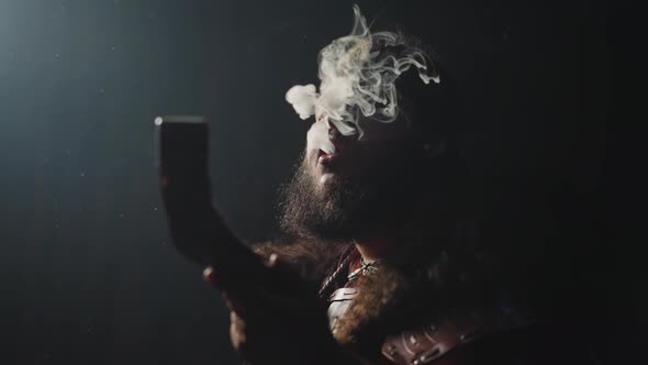 Bearded Man in Shaman Clothes Breathes Out Smoke on Black