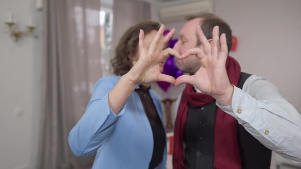 Couple Hands Forming Heart Shape with Happy Loving Man and Woman Kissing and Looking at Camera at