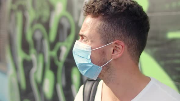 Cute Young Man in a White Tshirt and a Protective Mask in the City on a Graffiti Background