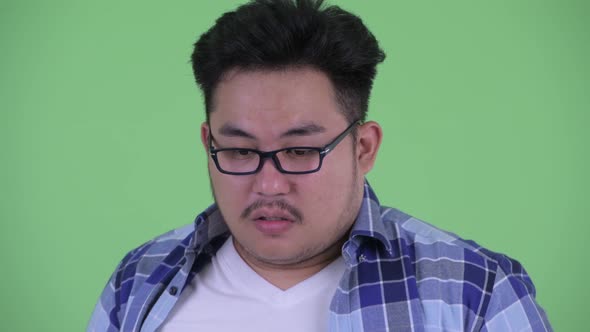 Face of Stressed Young Overweight Asian Hipster Man Thinking and Looking Down