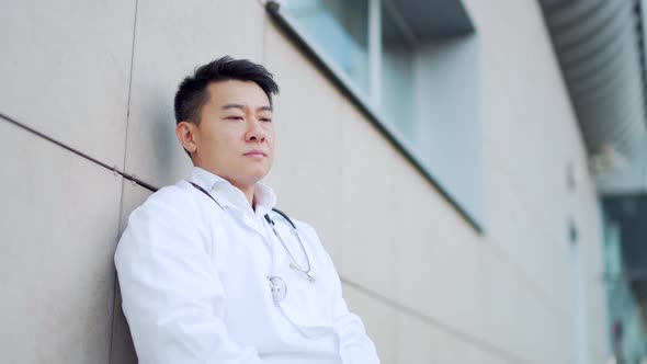 portrait stressful Asian doctor sitting or standing outside a hospital 