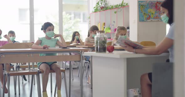 Children in the Classroom at School in Masks Sit in the Classroom and Listening the Teacher