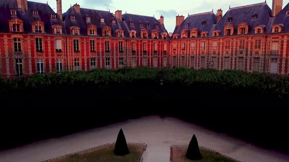 Uniform houses in corner of Place des Vosges illuminated by red light from rising sun. Ascending dro