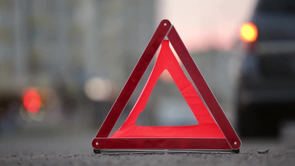 Red emergency stop sign behind broken blurred car with blinking lights on evening city street curb.