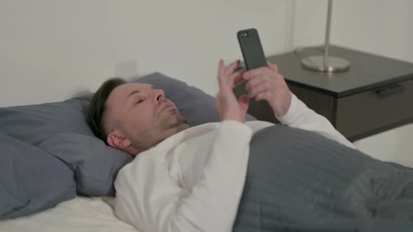 Casual Man Using Smartphone While Sleeping in Bed