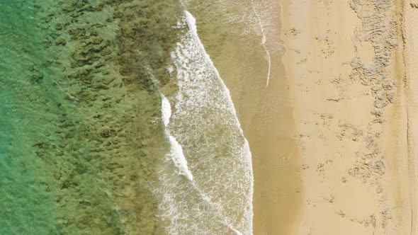 Aerial is ascending revealing 2 people taking a walk on the Beach of Porto Santo Island