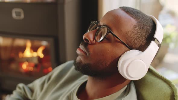 Relaxed Black Man Listening to Music with Headphones by Fireplace