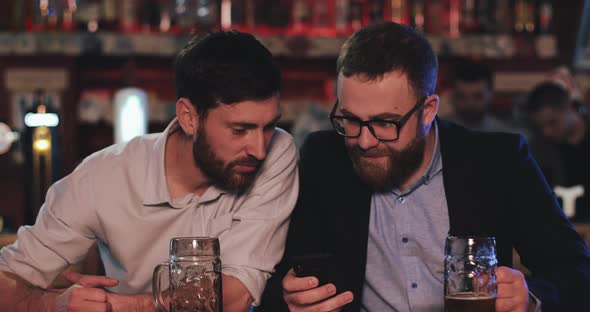 Two Old Friends with Smartphone Talking in the Beer Pub at Night