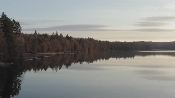 Aerial Sunrise over lake shoreline forestry melting ice on water surface