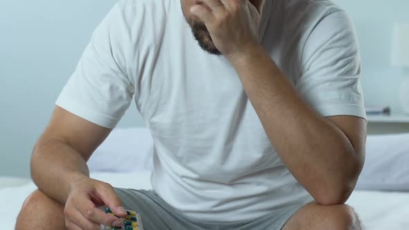 Sad Handsome Man Sitting on Bed Holding Pills Blister, Mens Health Problem