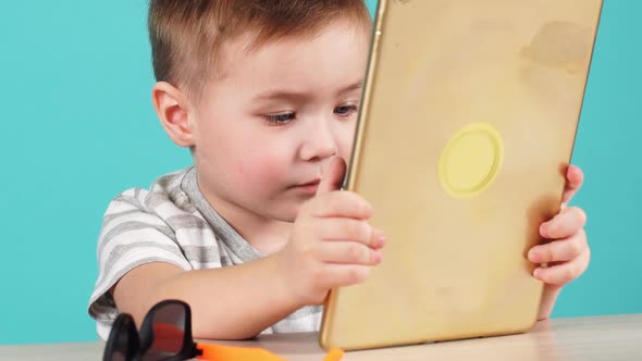 Close Up Face Cute Little Child Uses a Tablet PC Sitting at Table, Isolated on Blue