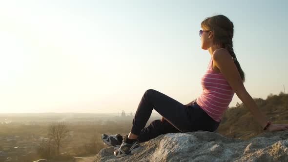 Young relaxed woman sitting outdoors on a big stone enjoying warm summer day. Girl meditating