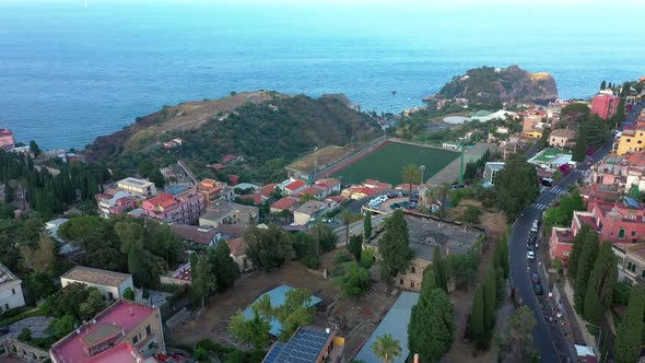 Aerial view of green hills carpeted with buildings and the Mediterranean sea in the background. Taor