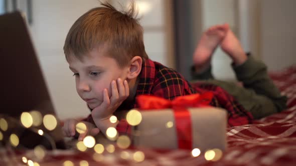 Cute Caucasian Boy Laying on Bed with Laptop Looking for Christmas Present