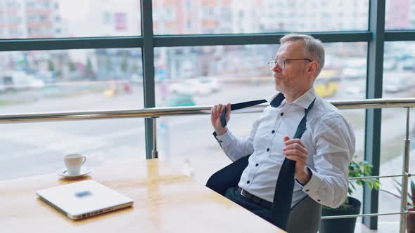 Senior businessman wears white shirt and drinking coffee near big window with city view 