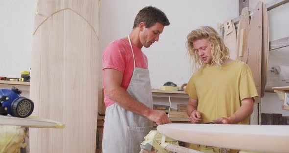 Two Caucasian male surfboard makers discussing the project with surfboards in the background
