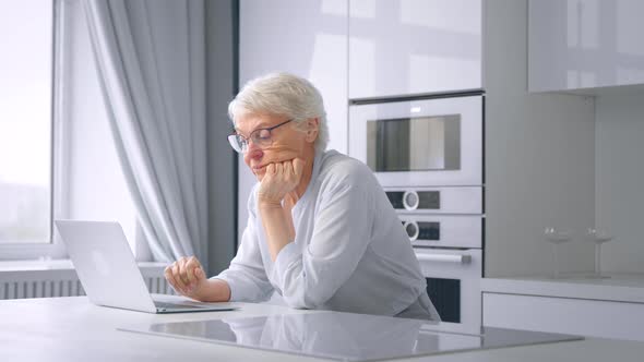 Exhausted old businesswoman takes glasses off after typing on laptop